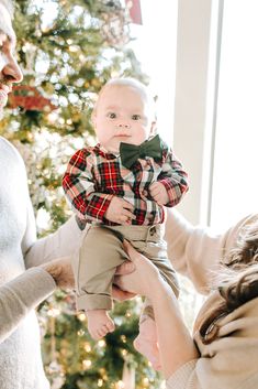 a woman holding a baby in front of a christmas tree