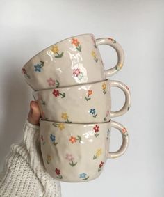 three coffee mugs are stacked on top of each other, one being held up by a woman's hand