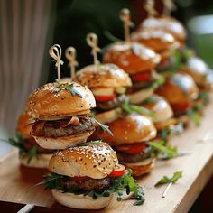 a row of mini hamburgers with tiny toothpicks on them sitting on a wooden table