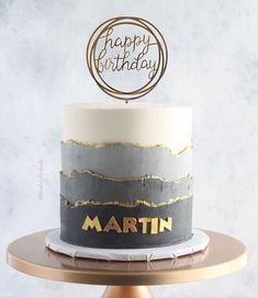 a birthday cake that is decorated with gold and grey frosting on a wooden stand