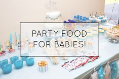 a party food table for babies with blue cups and desserts on the table in front of it