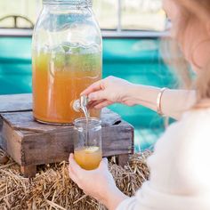 a woman pours a drink into a mason jar with straw bales around it