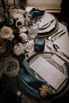 the table is set with silverware and blue napkins, plates, and flowers