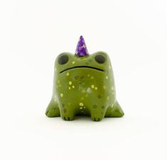 a green frog with a purple hat on it's head and eyes are sitting in front of a white background