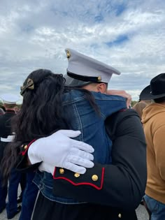 a man in uniform hugs a woman with long black hair while other people stand behind him