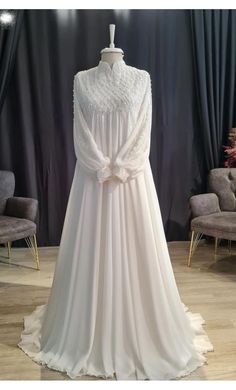 a white wedding dress on display in front of a black curtained room with chairs