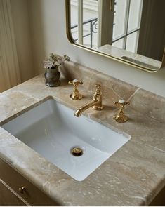 a bathroom sink with gold faucets and marble counter top next to a mirror