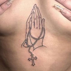 a woman's chest with a rosary and praying hands tattoo on her left side