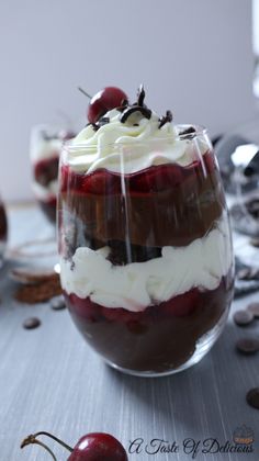 a dessert with cherries and whipped cream in a glass on top of a table