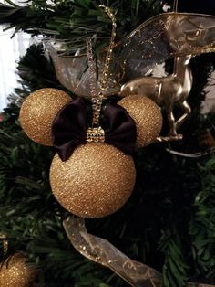 a mickey mouse ornament hanging from a christmas tree with gold and black ornaments