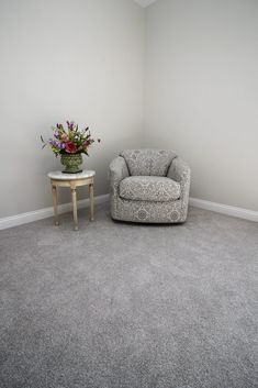 a living room with a chair, table and flower vase on the floor in front of it