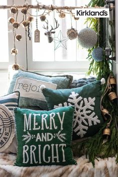 christmas pillows on a bed in front of a window with lights and ornaments hanging from the ceiling