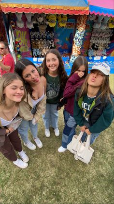 some girls are standing in front of a carnival booth and smiling at the camera while one girl is holding a white bag