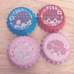 three bottle caps with cartoon characters on them sitting on a wooden surface, one is pink and the other is blue