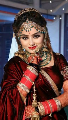 a woman wearing a red and gold bridal outfit with jewelry on her head, holding a