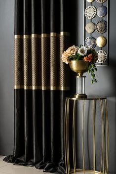 a gold vase with flowers in it next to a black curtain