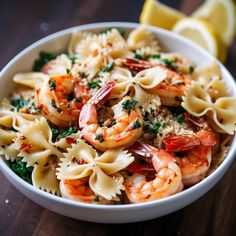 a bowl filled with pasta and shrimp on top of a table next to lemon wedges