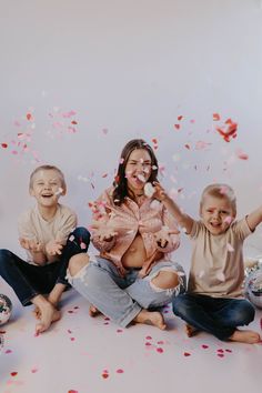 a woman and two children sitting on the floor with confetti in front of them