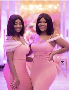 two women in pink dresses standing next to each other with their hands on their hips