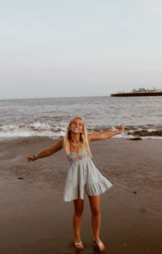 a woman standing on top of a sandy beach next to the ocean with her arms outstretched