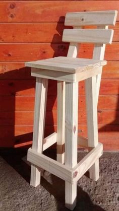 a white wooden chair sitting in front of a red wood wall with a shadow on the ground