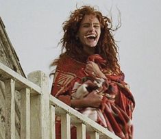 a woman with red hair is standing on a balcony and laughing at the camera man