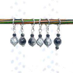 four silver and black beaded earrings hanging from a wooden stick on a white background