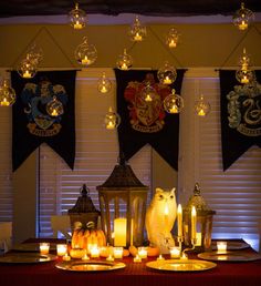 a table topped with lots of candles next to windows covered in banners and hanging from the ceiling