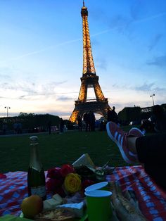 the eiffel tower is lit up at night, with food and drinks laid out in front