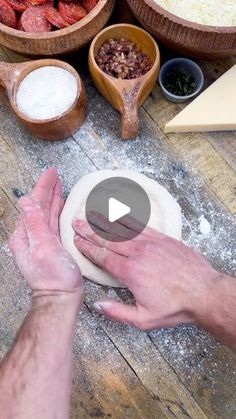 a person kneading dough on top of a wooden table next to bowls with food