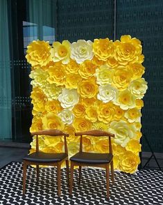 two chairs sitting in front of a yellow flower wall with large flowers on the side