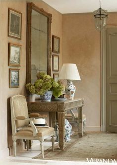 a room with a table, chair and mirror in the corner next to a lamp