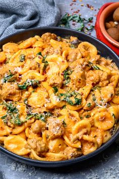 a bowl full of pasta with meat and spinach on the side next to nuts