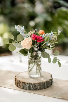 a vase filled with flowers sitting on top of a wooden slice covered in greenery