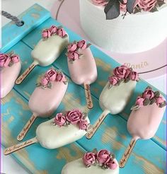 pink and white cake pops with flowers on them sitting on a blue tray next to a cupcake