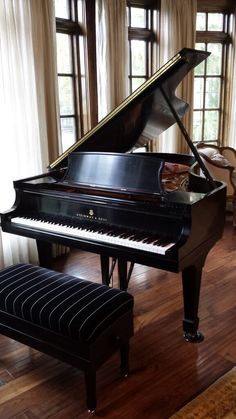 a grand piano sitting in the middle of a living room next to a bench and windows