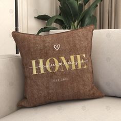 a pillow with the word home on it sitting on a couch next to a potted plant