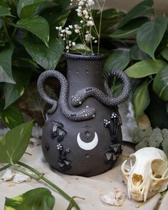 a vase with an octopus decoration on it next to a skull and some plants in the background