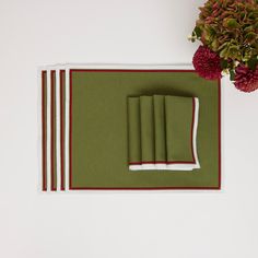 placemats and napkins on a table with flowers in the background, including red carnations