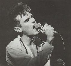 a young man singing into a microphone while wearing a shirt and beaded necklaces