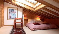 a bed sitting under a skylight in a bedroom next to a wooden wall and ceiling