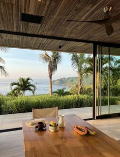 a wooden table with fruit on it in front of a window overlooking the ocean and palm trees