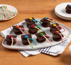 chocolate desserts are arranged on white plates with colorful candies and candy sticks in the middle