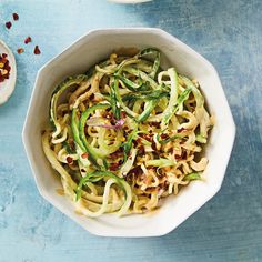 a white bowl filled with noodles and vegetables on top of a blue table next to a spoon