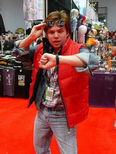 a young man wearing sunglasses and a vest pointing at the camera with his hand on his head