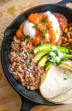 a skillet filled with beans, avocado, and other foods on top of a wooden table