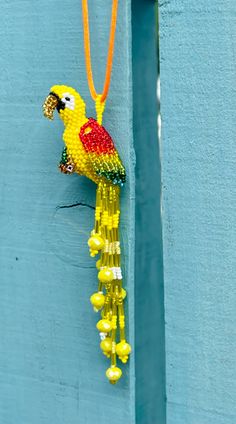 a beaded parrot hanging from a blue wall with beads on it's neck