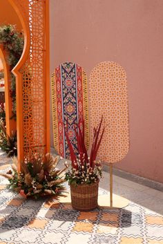 some plants are in a basket on the ground next to an orange wall with decorative designs