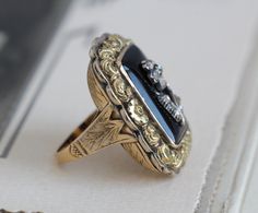 "A dramatic antique Victorian ring crafted in 14k yellow gold and sterling silver featuring a bezel-set black onyx face mounted with a sweet little silver pansy studded with rose-cut diamonds. It's possible this was originally a mourning brooch (the fabulously chased border is straight out of the Regency era circa 1820-30) that was converted to a ring later in the 19th century; it's beautifully executed and a fine testament to the Victorian jeweler's skill. Measuring approximately hair under 1 1 Victorian Black Enamel Anniversary Rings, Victorian Black Enamel Rings For Anniversary, Victorian Black Enamel Wedding Rings, Heirloom Black Enamel Rings For Wedding, Heirloom Black Enamel Wedding Rings, Victorian Black Enamel 14k Gold Rings, Victorian 14k Gold Rings With Black Enamel, Antique Black Rings With Rose Cut Diamonds, Vintage Black Rings With Rose Cut Diamonds