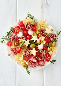 pasta salad with tomatoes, olives and cheese on a white platter against a wooden background